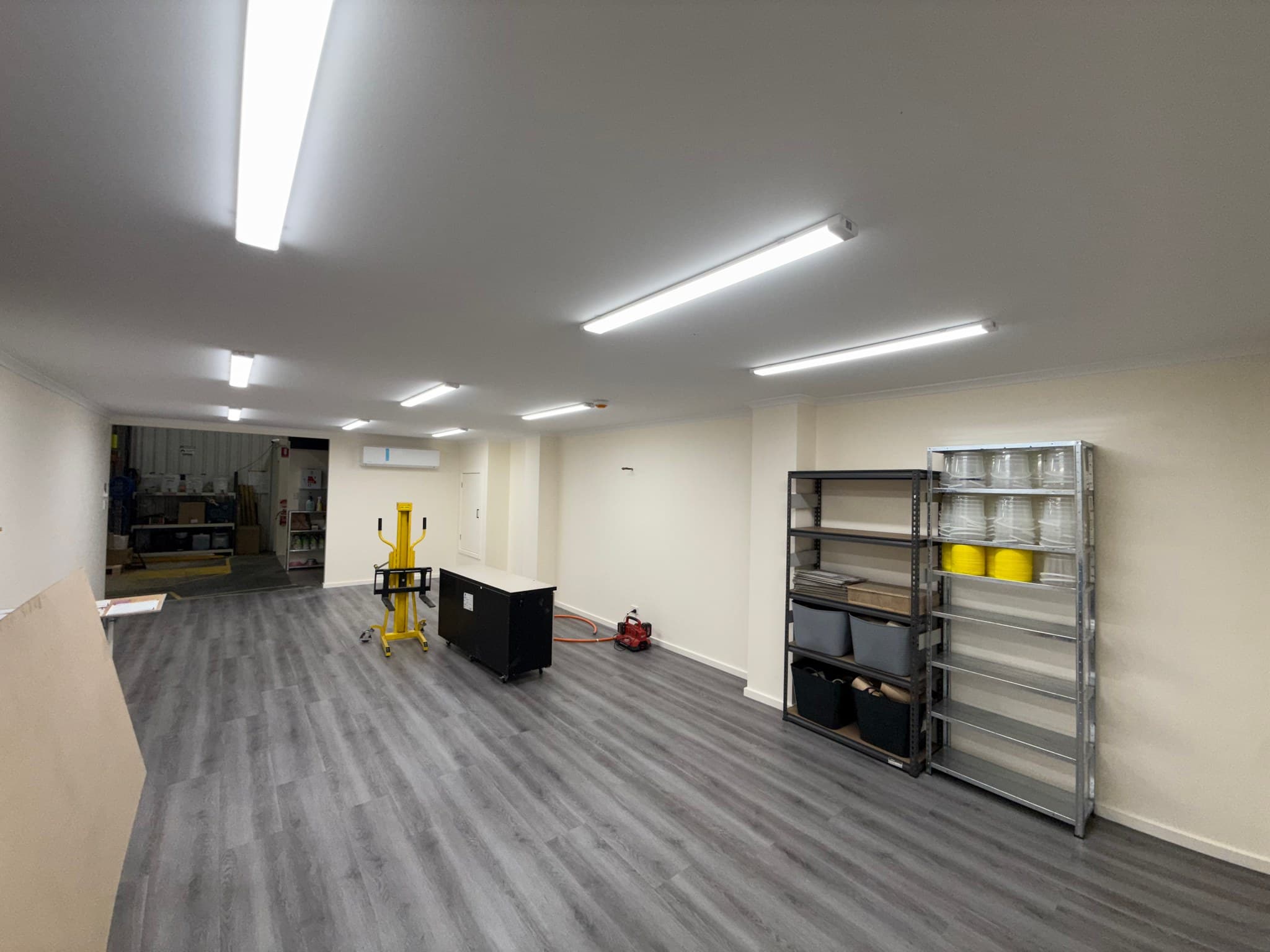 Commercial interior with illuminated ceiling battens, storage shelving and work equipment.