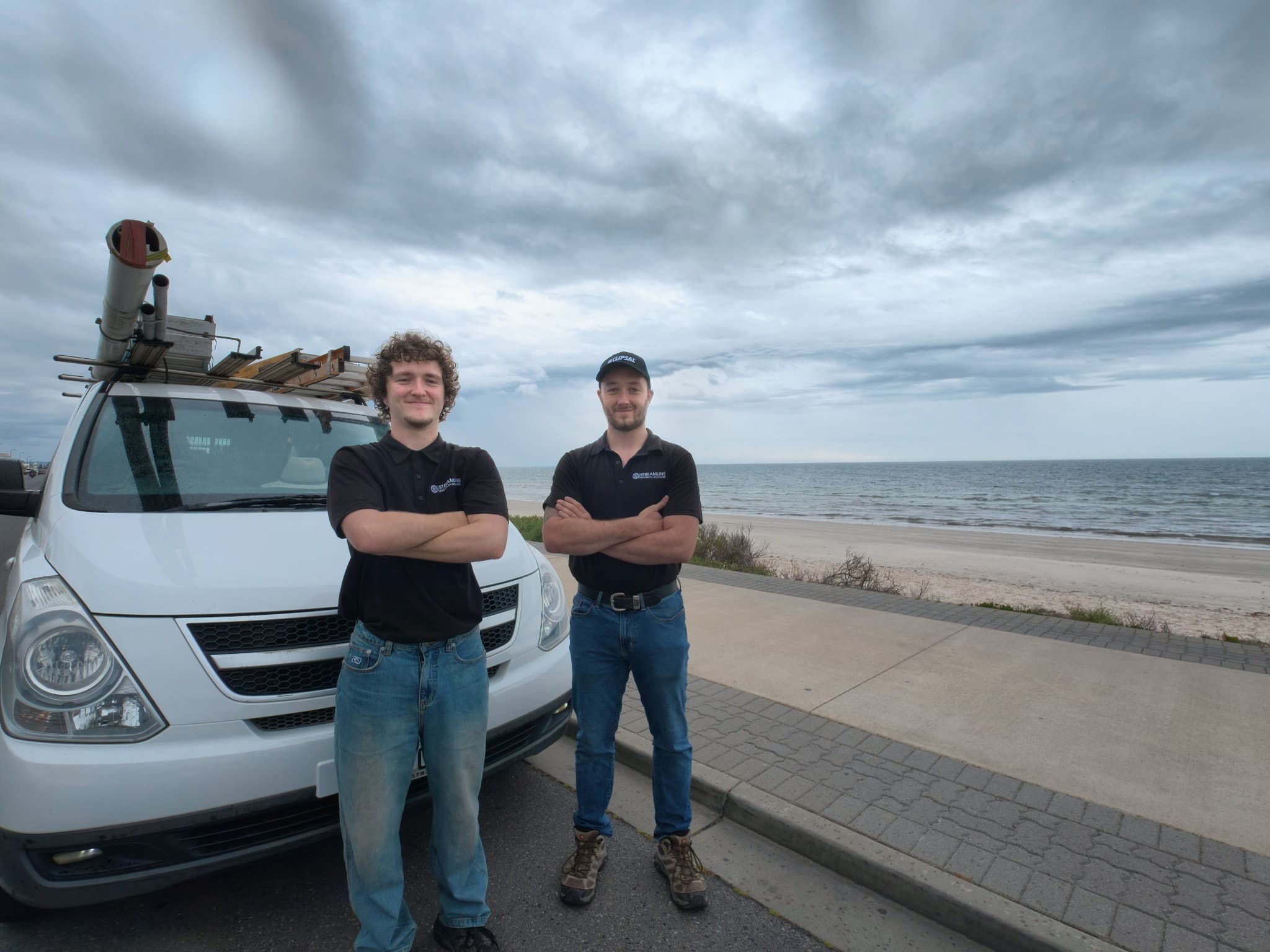 Paris and Nate standing beside the Streamline work van by the coast.